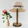 A hat displayed on a wooden stand next to a flower in a vase. Produktbild-Vorschau