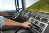 A person's hand is shown inserting a CD into the dashboard of a truck while driving on a scenic road. Podgląd zdjęcia produktu