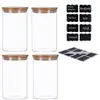Four clear glass jars with bamboo lids are arranged in a two-by-two grid. To the right of the jars are sheets of black chalkboard-style stickers with white text and a white chalk pen. Produktbild-Vorschau