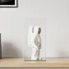 A white astronaut figurine inside a clear display case, placed on a wooden shelf against a white wall. Náhled obrázku produktu