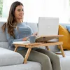 A woman is sitting on a couch using a laptop on a portable table. Produktbild-Vorschau