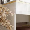 A close-up view of a modern vanity table with a gold trim, featuring a decorative dried plant. Produktbild-Vorschau
