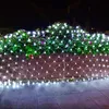 A string of white net lights is draped over a hedge and a wooden fence at night. Produktbild-Vorschau