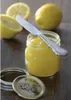 A jar of lemon curd with lemons and a knife on a wooden surface. Produktbild-Vorschau