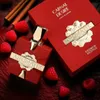 A red perfume bottle and its red packaging are displayed with raspberries and cinnamon sticks. Voir les images du produit