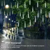 Outdoor scene at night with rain, featuring decorative lights on trees and a wet street. Náhľad obrázku produktu