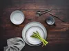 A table setting with plates, cutlery, a mug, and asparagus on a wooden table. Produktbild-Vorschau