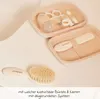 A baby grooming kit with a brush, comb, nail clippers, scissors, and a thermometer in a pink case, with an additional brush in the foreground. Produktbild-Vorschau