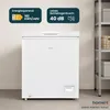 A white chest freezer is shown in a room with a shelf unit in the background. There are informational labels on the wall above the freezer. Produktbild-Vorschau