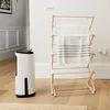 A white dehumidifier and a wooden drying rack with towels are shown in a room. Náhled obrázku produktu