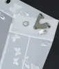 A close-up view of a white sheer curtain with a butterfly pattern, showing the grommets and a clip attached to the top edge. Produktbild-Vorschau