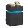 A dark gray, modern bedside table with three drawers and built-in blue LED lighting, shown in a studio setting with a vase of flowers and books on top. Podgląd zdjęcia produktu