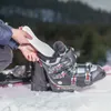 A person is inserting an insole into a ski boot, with skis visible in the background. Voir les images du produit