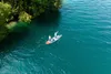 Two people paddleboarding on a clear turquoise lake next to a lush green treeline. Voir les images du produit