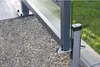 A close-up view of a gate stopper mechanism with a glass panel and metal frame, set against a backdrop of gravel and grass. Produktbild-Vorschau