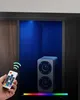 A hand holding a remote control points towards a small speaker in a cabinet lit by blue LED lights. Produktbild-Vorschau