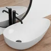 A white oval countertop sink with black faucets is shown on a wooden floor, with a reflection in a mirror. Anteprima dell’immagine prodotto