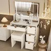 A white vanity table with a lighted mirror, drawers, and a stool, set in a bedroom. Produktbild-Vorschau