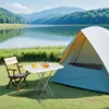 A camping scene with a tent, chair, and table set up near a lake. Produktbild-Vorschau