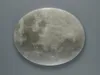 A close-up, top-down view of a round, decorative object resembling the moon, set against a plain gray background. Náhled obrázku produktu