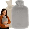 A woman is holding a grey plush hot water bottle, with a beige rubber hot water bottle and a grey plush hot water bottle visible in the background. Náhled obrázku produktu