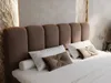 A close-up view of a bed with a brown upholstered headboard and white bedding. Produktbild-Vorschau