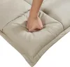 A hand is pressing into a beige upholstered floor seat, demonstrating its softness and cushioning. Voir les images du produit