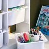 A white storage unit for children's items, with various bins and containers filled with art supplies and toys. Produktbild-Vorschau