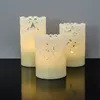 Three LED candles with intricate cut-out patterns are displayed on a reflective black surface against a gray wall. Produktbild-Vorschau