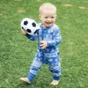A baby holding a toy soccer ball while standing on grass. Produktbild-Vorschau