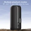 A black portable speaker is shown outdoors on a rocky surface with a blue sky in the background. Produktbild-Vorschau