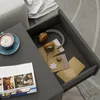 A drawer is open, revealing headphones and papers inside. A coffee cup and magazine are on the table next to the drawer. Voir les images du produit