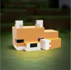 A stylized, blocky fox figurine, resembling a Minecraft character, rests on a blurred green surface with a blurred background of green and brown. Anteprima dell’immagine prodotto