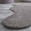 A close-up view of a fluffy, grey rug with a unique, scalloped edge, lying on a light grey wooden floor. A portion of a textured, purple ottoman is visible in the background. Produktbild-Vorschau