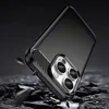 A black carbon fiber phone case with a triple camera cutout is shown in a dramatic, low-angle shot against a dark, rocky background. Small pieces of debris are flying around the case, suggesting it is being dropped or has just been dropped. Podgląd zdjęcia produktu