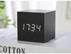 A black wooden cube digital clock displaying the time 17:34 sits on top of a book. Produktbild-Vorschau