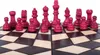 A close-up, diagonal view of a set of red chess pieces on a wooden chessboard. Anteprima dell’immagine prodotto