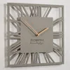 A modern square wall clock with Roman numerals and gold hands, displayed against a white background. Náhled obrázku produktu