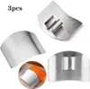 Three stainless steel finger guards for kitchen use, with one guard shown protecting a finger while slicing carrots. Produktbild-Vorschau