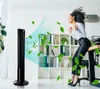 A woman is enjoying the cool air from a tower fan in an office setting, with leaves scattered around. Anteprima dell’immagine prodotto