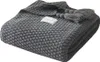 A folded gray knitted blanket with tassels and a small white label. Produktbild-Vorschau