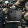 A black portable cooler sits on a rocky shore next to a metallic water bottle. Podgląd zdjęcia produktu