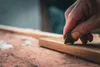 A close-up shot of a hand using a scraping tool on a wooden surface. Produktbild-Vorschau