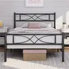 A black metal bed frame with a decorative headboard and footboard, set up in a bedroom with bedding and pillows. Produktbild-Vorschau