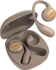 A pair of beige wireless earbuds and their charging case are shown against a light gray background. One earbud is outside the case, attached to a curved band that goes over the ear. The charging case is open, revealing the interior where the earbuds are st Voir les images du produit