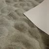 A close-up view of a textured surface, likely sand, with a light-colored rectangular object partially covering the right side. Náhled obrázku produktu
