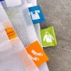 Close-up of mesh laundry bags with colored tags indicating clothing types. Voir les images du produit