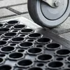 A close-up view of a black rubber mat with circular cutouts, with a gray wheel resting on its edge. Podgląd zdjęcia produktu