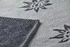 A close-up view of a gray blanket with a dark gray embroidered edelweiss pattern and a dark gray border with white stitching. Produktbild-Vorschau