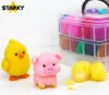 A yellow chick and a pink pig made of felt sit on a white surface, with a clear plastic container filled with colorful felt wool in the background. Two yellow felt balls are also visible in the foreground. Produktbild-Vorschau